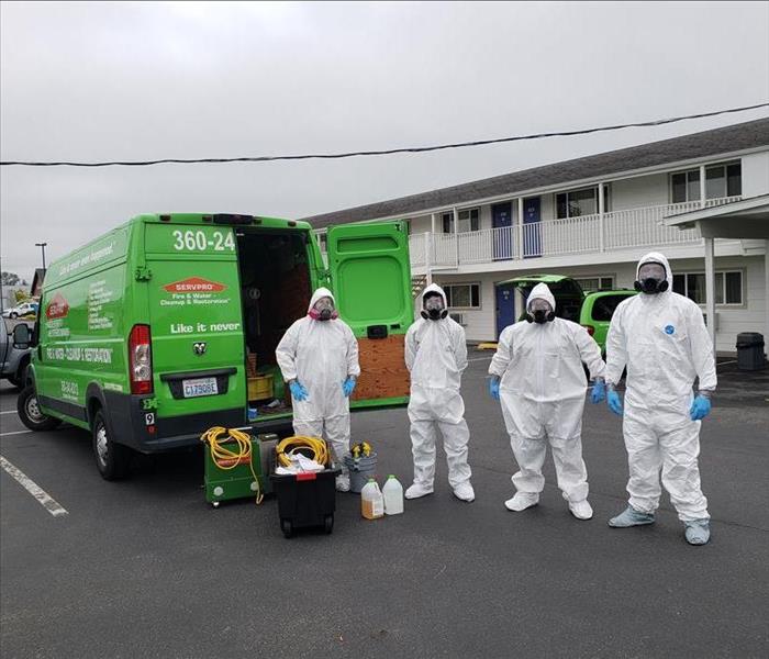 green SERVPRO van with 4 employees dressed in full PPE in front of a hotel
