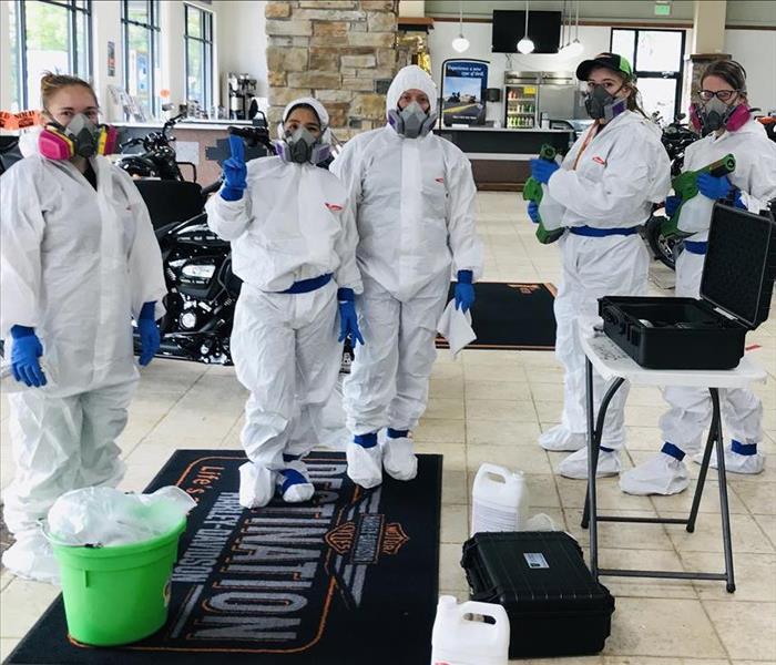 Five employees posing in hazmut suits, respirators and equipment inside showroom